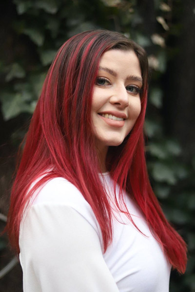 A young woman with red highlights in her hair is standing in a garden