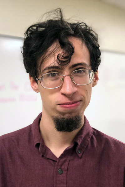 A portrait of a young man with a goatee in a classroom