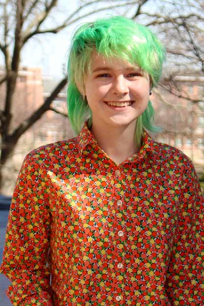 A young lady with green hair is smiling outside