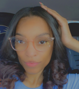 Shera wearing clear-rimmed glasses, looking directly at the camera with a slight smile.