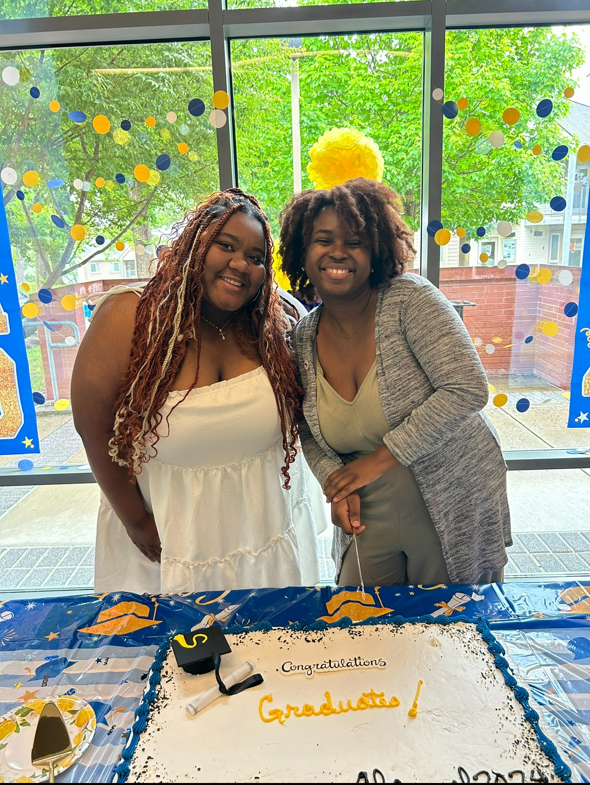 Kayla with another student standing behind a table decorated with graduation caps and cake
