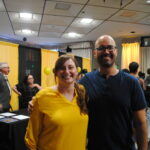 Samantha and Professor Arenas Gomez at a UMBC event. Samantha is wearing a yellow top and Professor Arenas Gomez is wearing a blue shirt. In the background you can see many faculty and students.