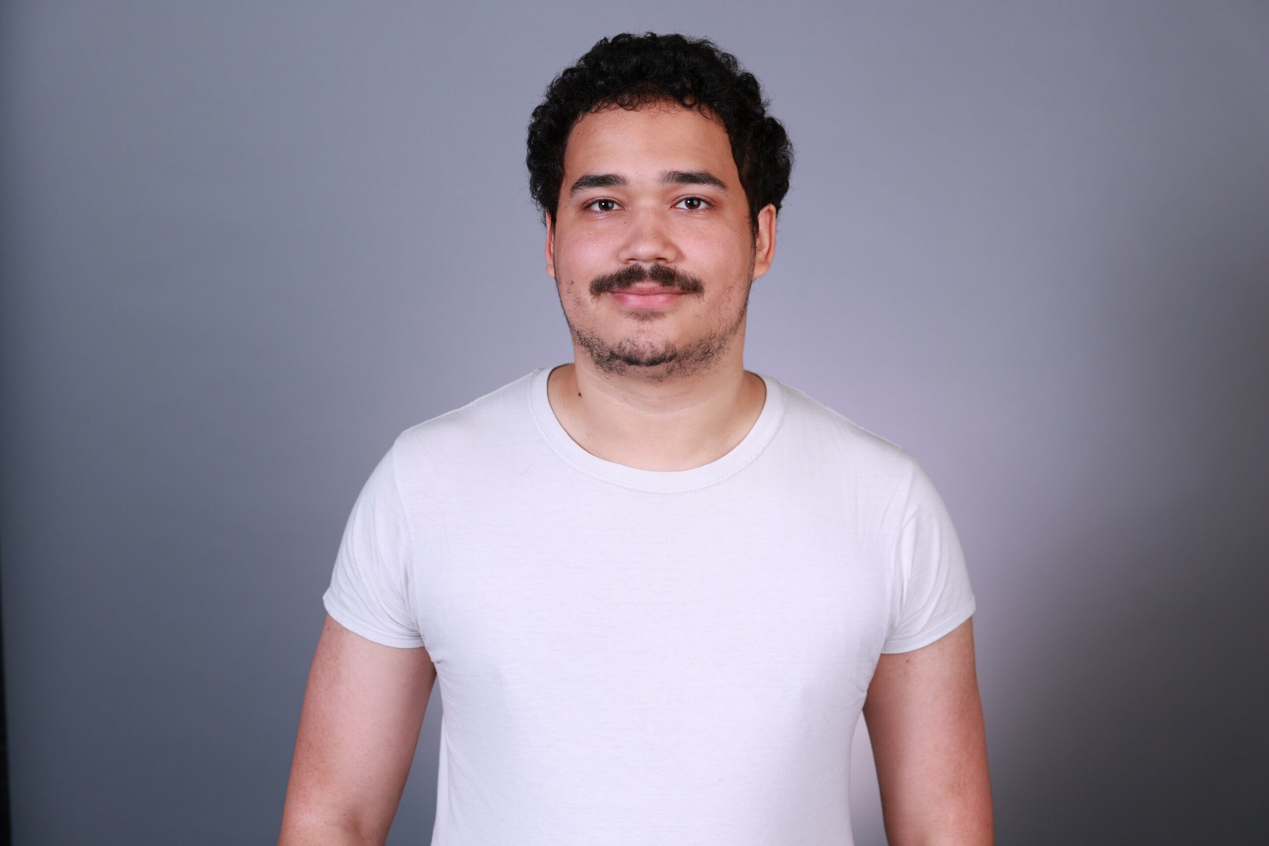 Alex standing in front of a gray background with white shirt