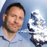 Cameron looking at the camera slightly smiling in a blue collar shirt. With photo design by his company